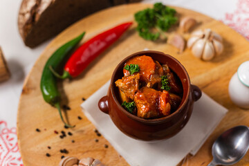 meat goulash in a ceramic pot on a wooden background