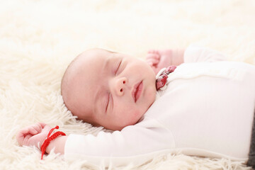 
7 day old baby sleeps happily in bed on a fluffy white blanket dressed in a white shirt and red bow tie in a white room