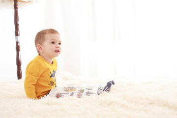 
3 year old child sitting on a white fluffy blanket in a white room and looking at a book happily