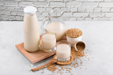 Vegan non diary buckwheat milk in glasses with buckwheat groats in a bowl on white stone table. Vegan buckwheat drink is plant based alternative milk . Veggies healthy milk product, selective focus