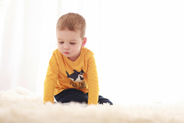 Naklejka premium 3 year old child sitting on a white fluffy blanket in a white room and looking at a book happily