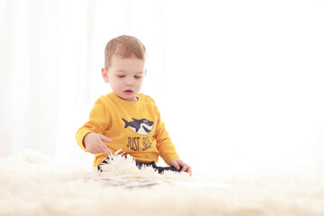 

3 year old baby sitting on a white fluffy blanket in a white room and looking around happily