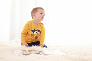 Fototapeta premium 3 year old baby sitting on a white fluffy blanket in a white room and looking around happily