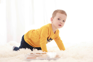 Naklejka premium3 year old baby sitting on a white fluffy blanket in a white room and looking around happily