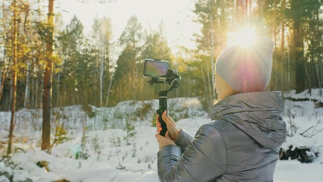 The Woman Professional Videographer Holding Smartphone on 3-axis Gimbal Stabilization Device in Winter. Pro Equipment Helps to Make High Quality Video on Phone. Cinematographer Operator. Slow Motion