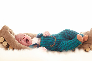 7-day-old baby is lying in bed on a fluffy brown brown  sitting in a wicker basket and looking around in a white room and wearing a blue fluffy T-shirt and jumpsuit