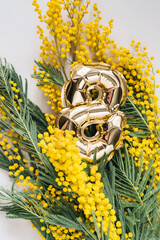 Golden balloon in the shape of 8 with a mimosa and a gift for the holiday. International Women's Day. March 8th. The power of women, women's month, feminism. Vertical photo.
