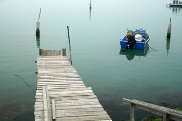 Molo di legno in prospettiva con barca colore blu in primo piano su sfondo di mare calmo e piatto
