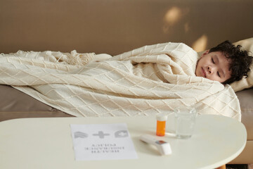Sick boy with fever sleeping on sofa in living room after taking prescribed medicine