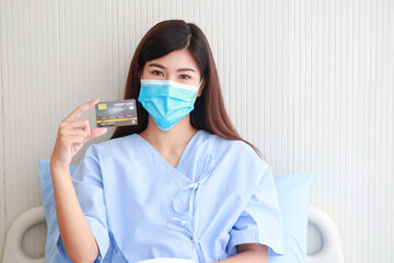 Beautiful Asian woman being treated in the hospital. She was wearing a hygienic mask sitting on her bed holding a credit card. Concept of medical services in hospitals. health insurance