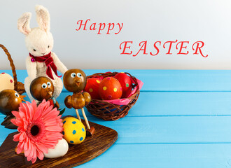 Spring and Easter holiday background with gerbera flowers, colorful pastel eggs, Bunny and Chicks on blue table. Happy Easter greeting card. Card with copy space for text.