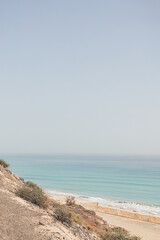 Picturesque seashore landscape with blue waves, green grass and beach sunbeds. Peaceful state of mind. Tranquility and serene relaxation concept. Ocean getaway.