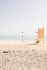 Yellow wooden rescue tower at the sand beach on a sunny summer day during. Sea, sky and green swimming flag background. Lifeguard station. Copy space. Vacation concept.