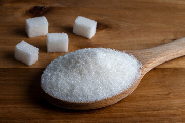Fototapeta na wymiar Granulated sugar and sugar cubes in wooden spoon on wooden background
