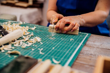 Fototapeta na wymiar A female carpenter cuts wood with a knife in a carpentry or makeshift workshop.