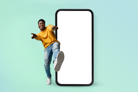 Hey you, check this website. Excited black man standing near huge smartphone with blank screen, mock up