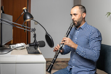 Young entrepreneur playing the clarinet at home and recording music to stream it online with his computer
