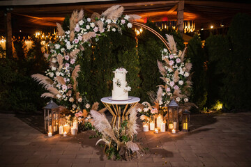 night wedding ceremony, the arch is decorated with flowers, candles and garlands of light bulbs and there is a wedding cake on the table