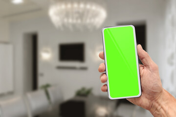 Male hand using mobile phone with smart home control application and green chromakey screen in living room