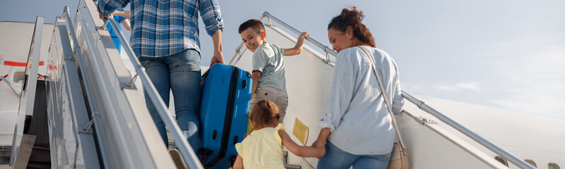 Back view of parents with two kids getting on, boarding the plane on a daytime, ready for summer...