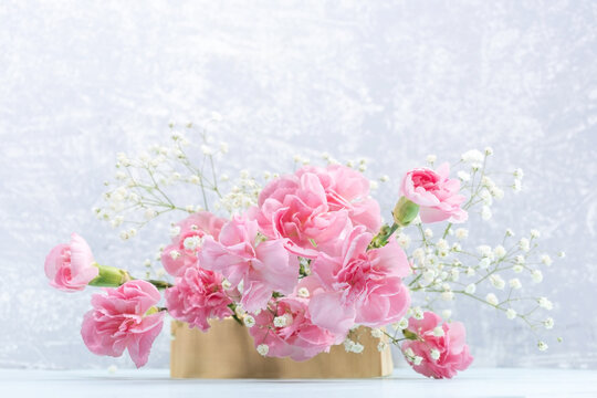 Pink carnations and white gypsophila flowers on wooden stand on light grey. Mother's Day card.