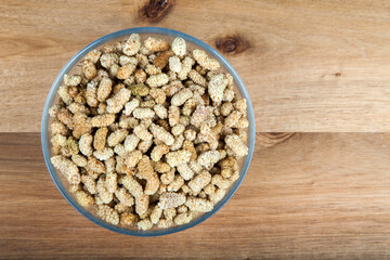 Dried mulberry in glass bowl on wooden background