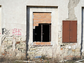 Wall of an old and abandoned building. We see a fallen plaster and a knocked out window.