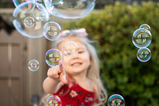 Little girl playing with bubbles. Happy child popping bubbles.