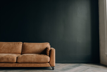 Brown sofa on a dark gray wall background. Conceptual photo of an interior with a place for an...