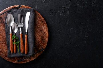 Vintage silverware. Rustic vintage set of wooden spoon and fork on wooden platter on black background. Empty dishes. Top view. Mock up.