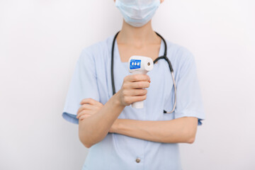 Temperature measurement gun in doctor hands. Close-up shot of doctor wearing protective surgical mask ready to use infrared isometric thermometer gun to check body temperature for virus symptoms