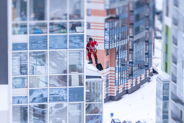 Professional climber rope access worker with a shovel removes snow and take off icicle from high rise building, industrial mountaineers working at heights, manual snow removal, cleaning the roofs