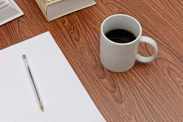 Desk with papers, books, pens and a cup of coffee on top.