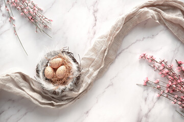 Easter background with eggs in nest on linen towel. Small pink Spring flowers on off white marble...