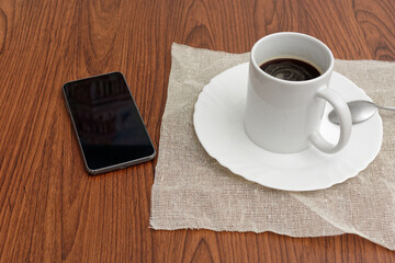 Fototapeta na wymiar Cup of coffee and cell phone on wooden table.