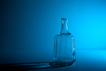 Glass bottle with copy space. Large creative vintage vase. Graphic still life with light and shadow in blue light. An art object. Recyclable material. The concept of alcoholism. Open flask