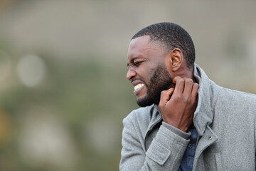 Stressed man with black skin scratching neck in winter