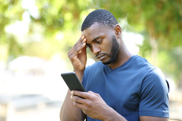 Worried man with black skin checking mobile phone in a park