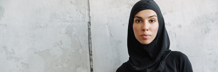 Young muslim woman in hijab standing with water bottle indoors