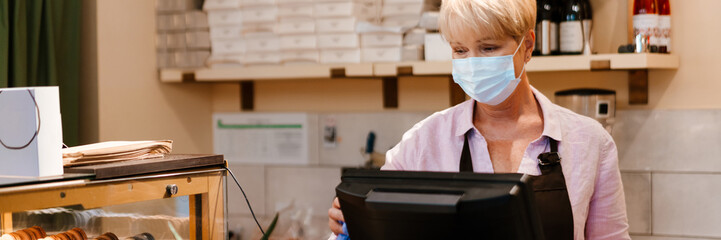 Mature woman wearing face mask working at cash register in cafe