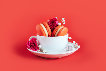 Red french macarons with rose flower in a cap on a red background.