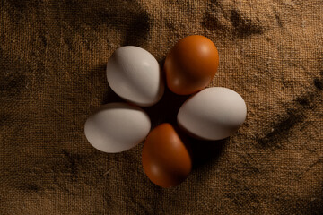 Five brown and white eggs are laid out in a circle, on a textured substrate with a beautiful texture. A few eggs, folded like chamomile petals, are lying on burlap, on Easter Eve.