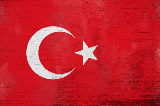 Full frame photo of a weathered flag of Turkey painted on a plastered brick wall.