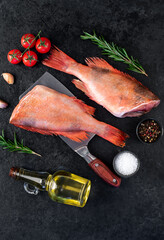 Raw red sea bass with rosemary and spices on a knife on a stone background