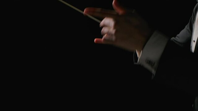 Symphony orchestra conductor wearing suit is directing musicians with movement of baton, isolated on black background. Conducting, directing a musical performance with visible gestures. Close up.