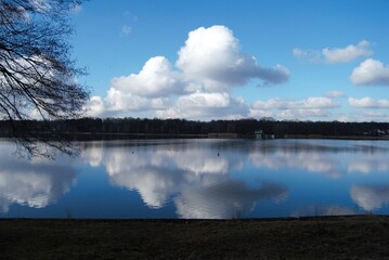 Białe chmury na tle błękitnego nieba odbijające się w tafli wody jeziora