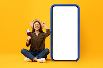 Female Tourist Sitting Near Big Cellphone Holding Passport, Yellow Background