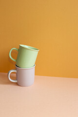 Stack of pastel color mug cup on pink table. orange wall background. copy space