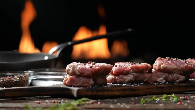Raw tenderloin steak meat beef sprinkled with salt and seasoning on wooden chopping board on a wooden table prepared for cooking with flames in the background. slow motion