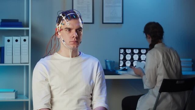 Man wearing EEG topographer for examining brain, doctor making electrogram of scalp activity. Researching of brain work using electroencephalography headset.